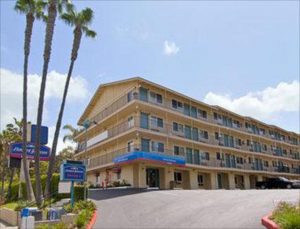 View of Howard Johnson hotel building with palm trees and parking area in San Diego
