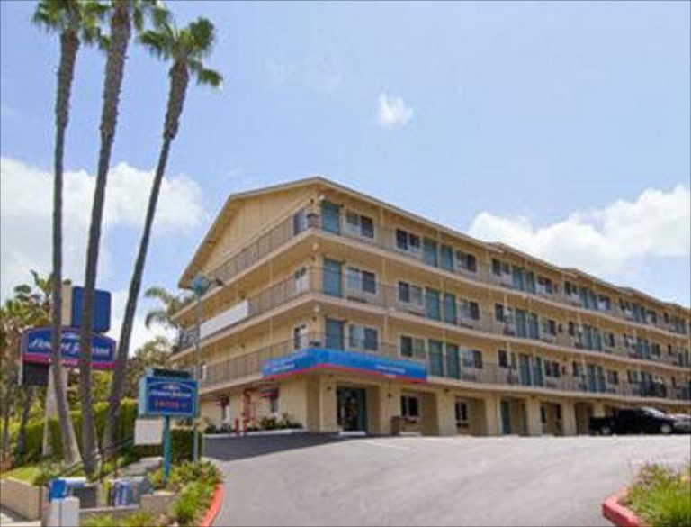 View of Howard Johnson hotel building with palm trees and parking area in San Diego