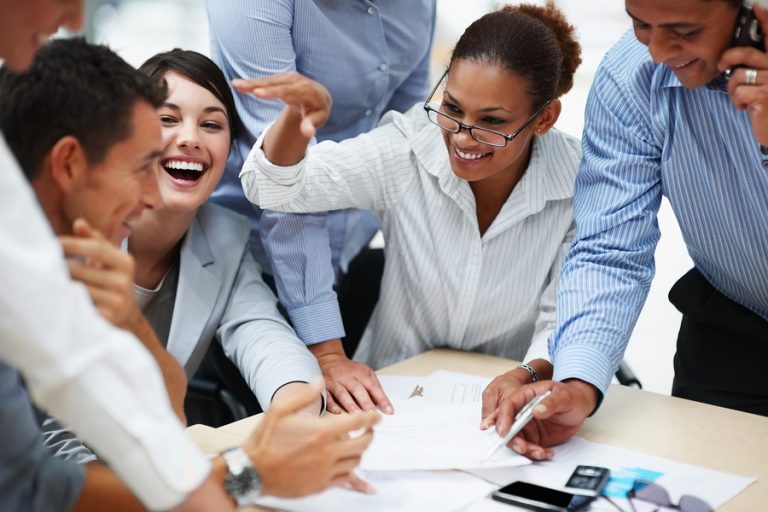 Group of smiling business professionals engaged in a meeting, discussing documents around a table
