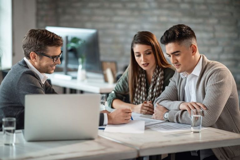 A young couple sits with a financial consultant reviewing investment plans during a meeting.